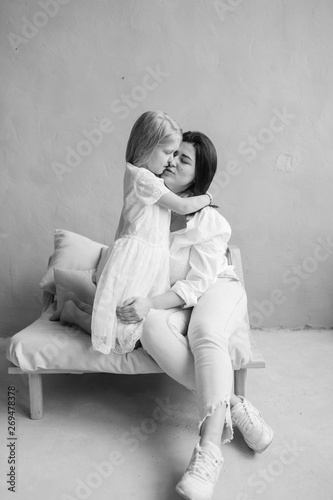 Mother and daughter indoor lifestyle black white portrait. Mom with child have fun in studio. Happiness of motherhood. Mother hugs with her little daughter. Young emotional girl embraces her mom.