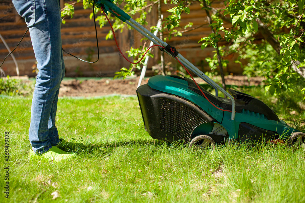 Young man mowing the lawn. Worker doing his job in backyard. Spending summer day in garden. Lawnmower standing on the background of private garden. Close up.. Young man mowing the lawn. Worker doing his job in backyard. Spending summer day in garden. Lawnmower standing on the background of private garden. Close up..
