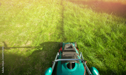 Close up of  lawn mower on green grass. Worker doing his job in backyard. Spending summer day in garden. Nobody..