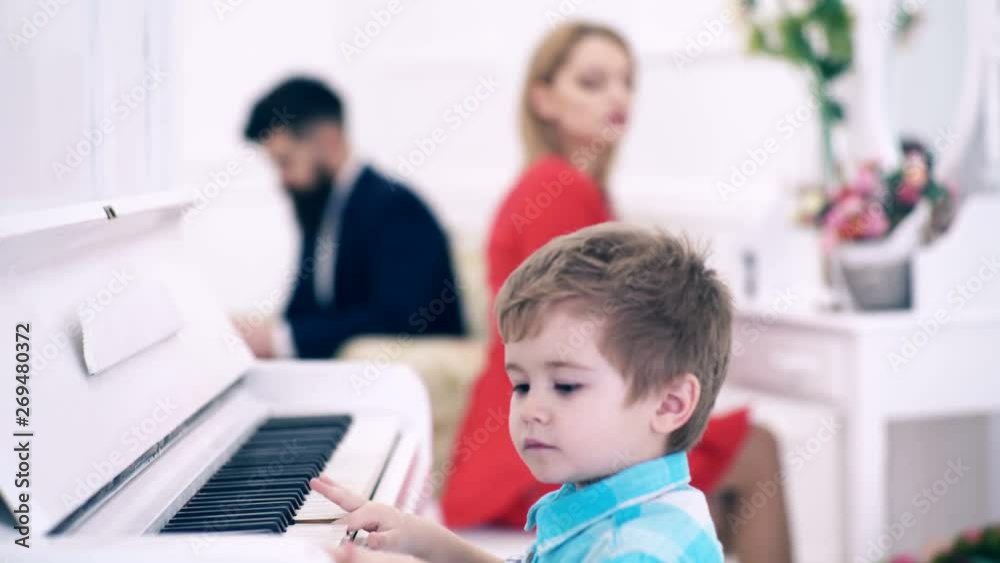 boy plays the piano, his mother makes make-up in front of the mirror and his father reads a book in an expensive white interior, transfer focus. Rich parents enjoy parenthood. Boy adorable play piano. boy plays the piano, his mother makes make-up in front of the mirror and his father reads a book in an expensive white interior, transfer focus. Rich parents enjoy parenthood. Boy adorable play piano.