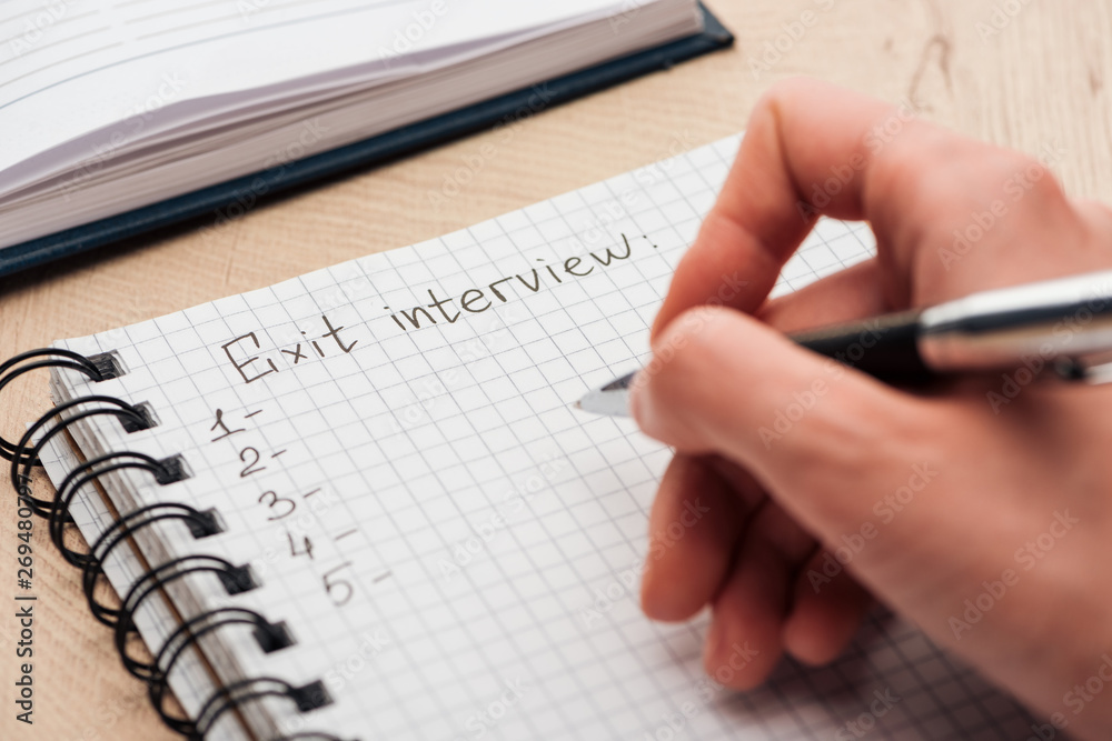 cropped view of recruiter writing in notebook with exit interview lettering cropped view of recruiter writing in notebook with exit interview lettering