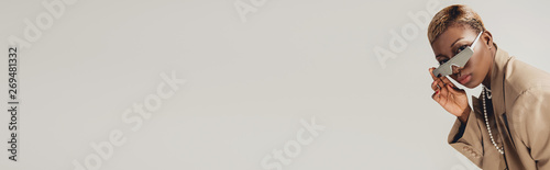 trendy african american girl posing in sunglasses and beige jacket isolated on grey