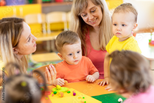 Babies with teacher play colorful clay toy in nursery