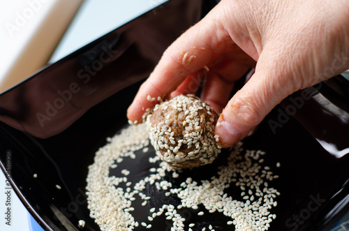raw food sweets roll in white sesame on a black plate with female hands