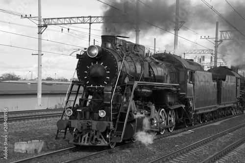 Black and white retro steam train in clouds of smoke rides by rail, rolling tourists