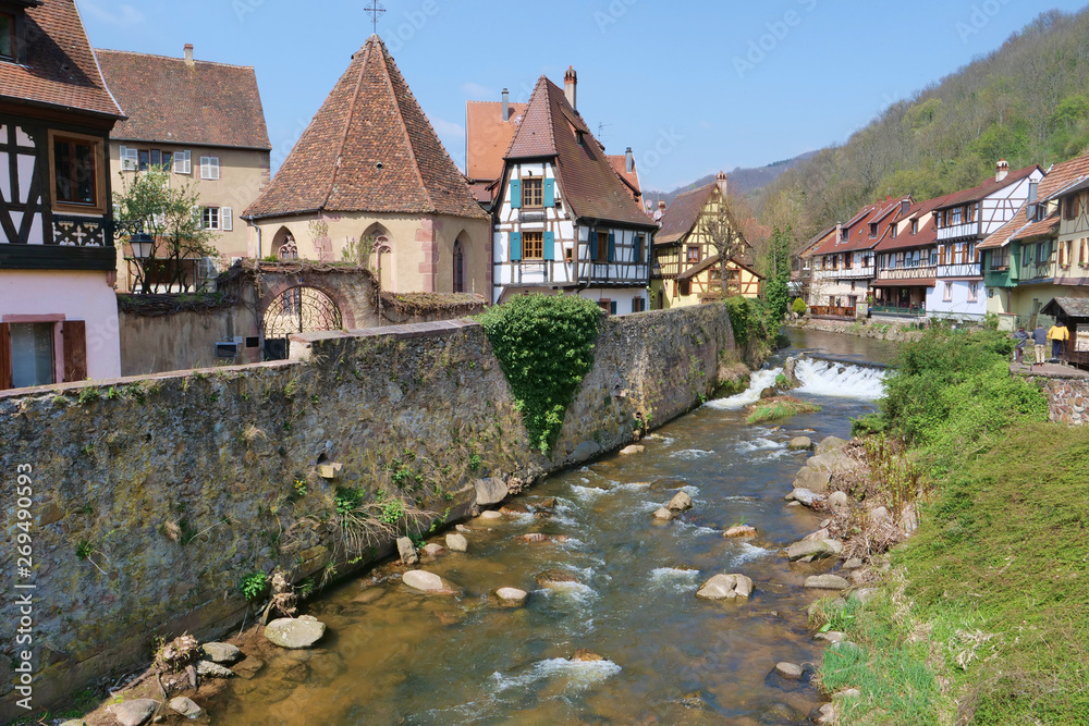 Medieval half-timbered houses behind an ancient wall next to a quiet stream