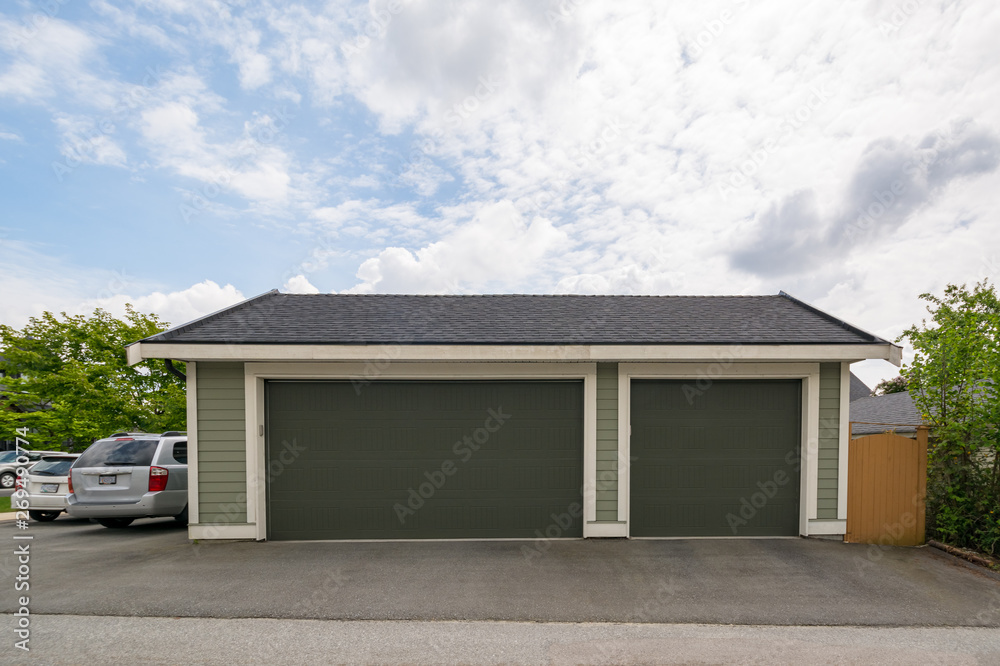 Detached wide garage for three cars parking. Back yard garage with two cars parcked beside on cloudy sky background Detached wide garage for three cars parking. Back yard garage with two cars parcked beside on cloudy sky background