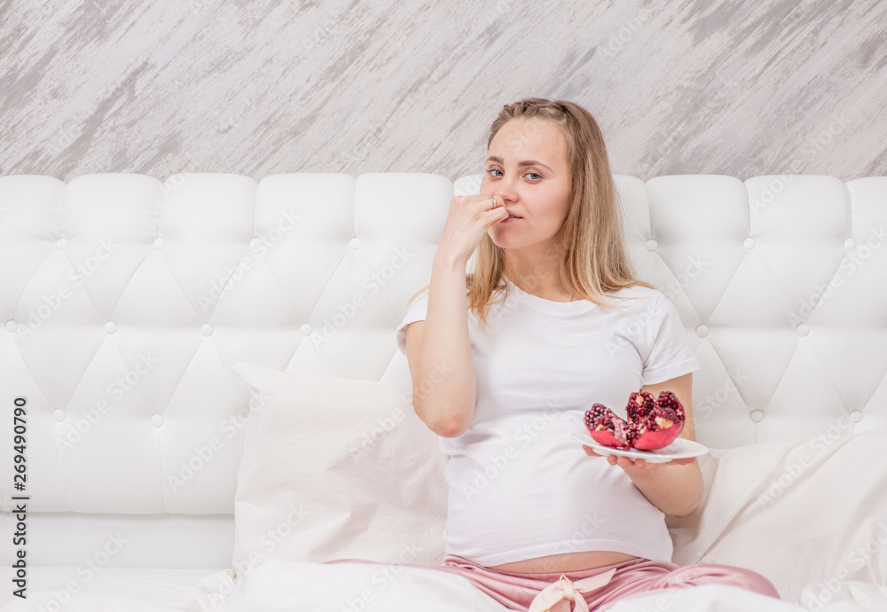 Young pregnant woman eating red pomegranate, to increase hemoglobin. Empty space for text Young pregnant woman eating red pomegranate, to increase hemoglobin. Empty space for text