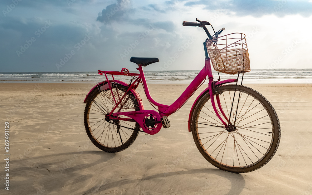 Fototapeta premium Pink colored old ladies bicycle parked on the isolated beach after cycling. A fun filled healthy activity and a must to do on the beach.