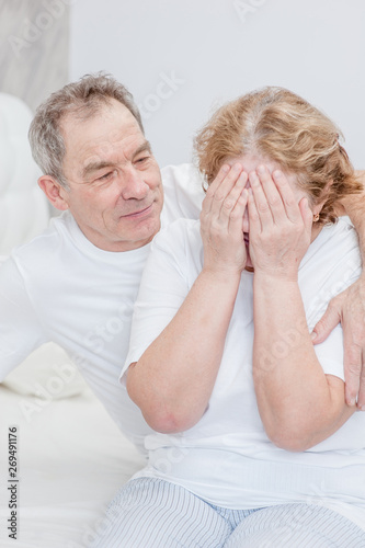 Senior man calms his crying wife at bedroom