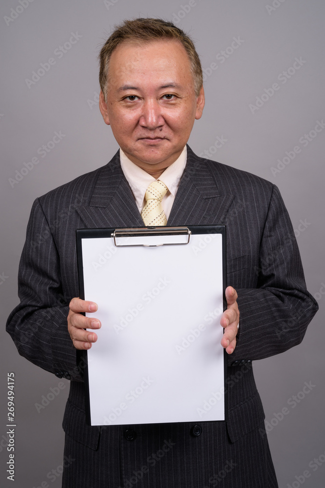 Portrait of mature Asian businessman against gray background Portrait of mature Asian businessman against gray background