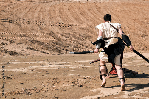 A concept photo of a Roman battle of two warriors of the Colosseum in action with aggressive emotions in full military uniform on a desert landscape on a sunny day with a dry sun.