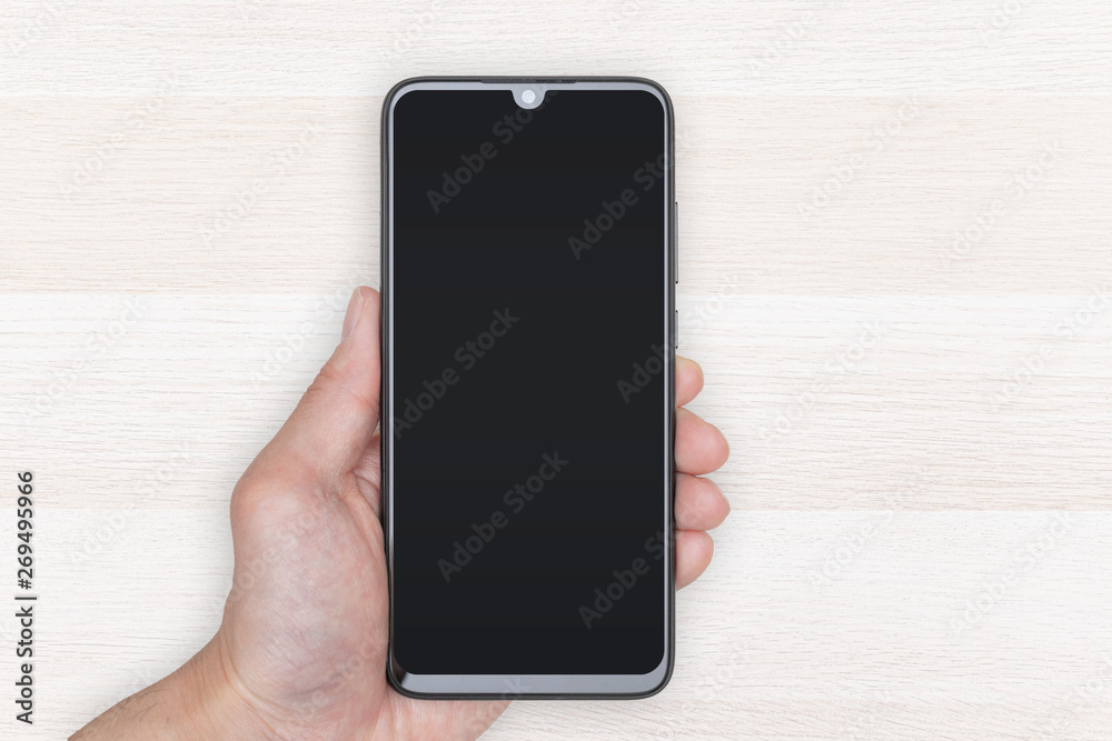 Hand Holding Mobile Phone on Light Wood Background in Vertical Position Hand Holding Mobile Phone on Light Wood Background in Vertical Position