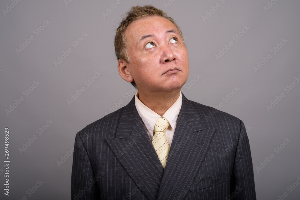 Portrait of mature Asian businessman against gray background Portrait of mature Asian businessman against gray background