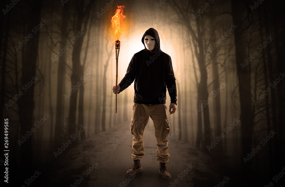 Obraz premium Mysterious man coming from a path in the forest with burning flambeau concept 