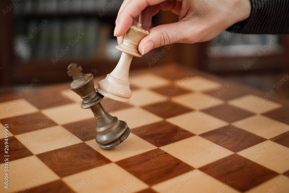 Concept: the woman who dominates the man. A woman's hand gives checkmate to  the king with the queen on a wooden chessboard, with no other pieces in  play Stock Photo