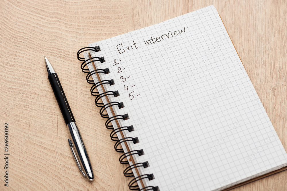 notebook with exit interview lettering, copy space and numbers on wooden table near pen notebook with exit interview lettering, copy space and numbers on wooden table near pen