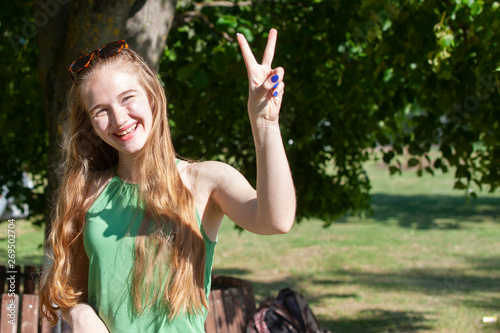 Cheerful girl making gun shot gesture. Beautiful young woman in casual enjoying leisure time in city park, turning round, smiling and gesturing at camera. Gesturing concept