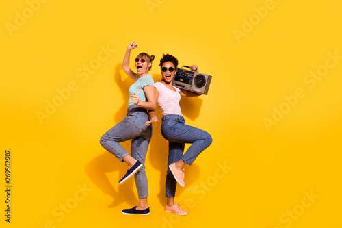 Full length body size view cheerful content enjoy active journey holiday beach sea summer retro hold hand sing wavy top-knot trendy style stylish t-shirt jeans specs legs isolated yellow background