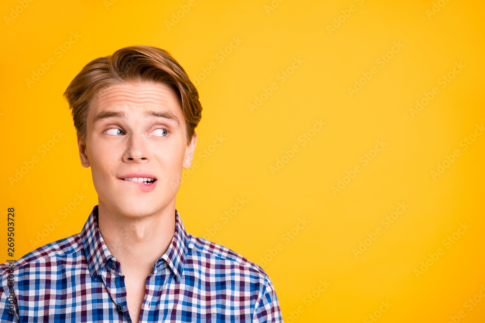 Close up photo amazing youngster he him his look side empty space bite teeth lower lip not sure have doubts choice choose wearing casual plaid checkered shirt outfit isolated yellow bright background
