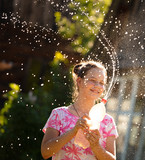 girl squeezes a bottle of water and blowing spray in the backlight of the sun. girl watering splashes of water from a bottle without a brand. joyful girl playing with splashes and streams of water.