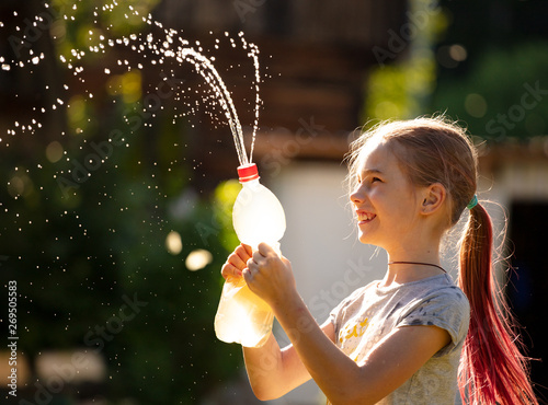 splashes and drops of water in the sunlight. girl watering splashes of water from a bottle without a brand. cheerful girl playing with spray and water jets. background with multi-colored spots