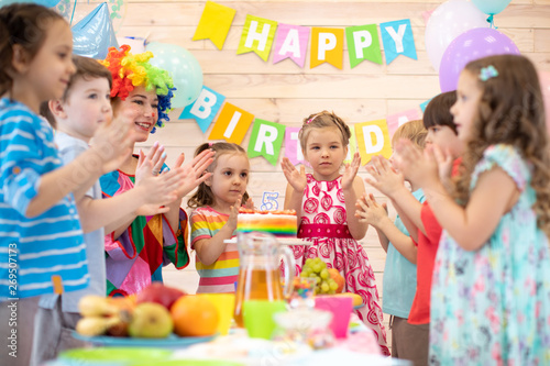Children group with clown clown clap around table with birthday cake