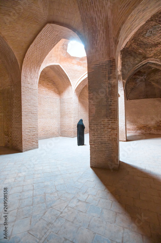 Jameh Mosque  praying hall with brick pillars of stones and roof - Muslim woman in headscarf and hijab prays in mosque