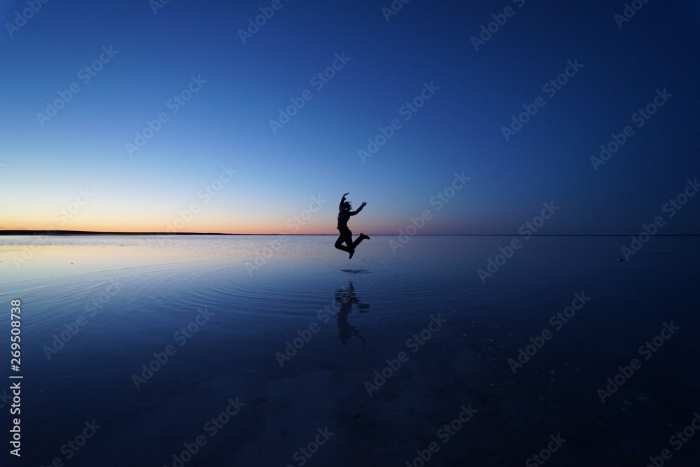Jumping silhouette reflection over a salt lake at blue hour