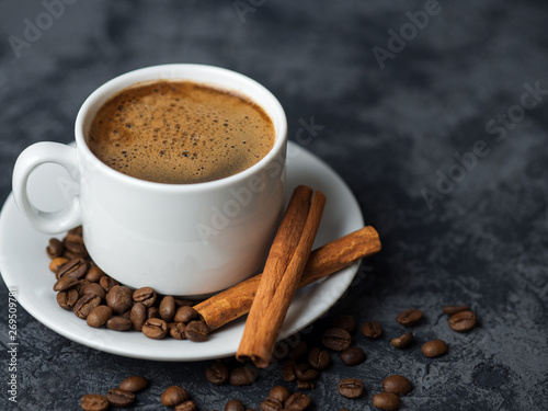 White espresso coffee Cup with cinnamon and coffee beans on dark concrete background