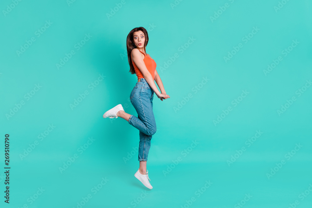 Full length side profile body size photo beautiful her she lady jump high amazed excited unexpected weekend vacation wear casual orange tank-top jeans denim isolated bright teal turquoise background