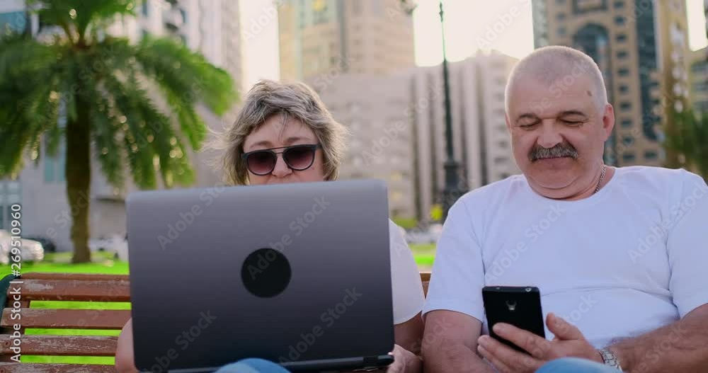 Senior couple using a laptop while sitting on chair in the park Senior couple using a laptop while sitting on chair in the park