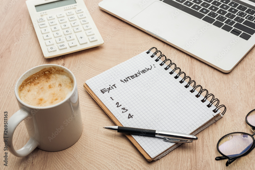 notebook with exit interview lettering and numbers on wooden table with laptop, stationery, glasses and cup of coffee notebook with exit interview lettering and numbers on wooden table with laptop, stationery, glasses and cup of coffee