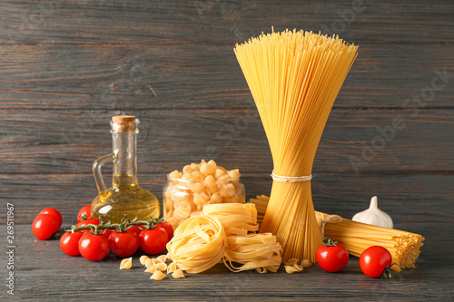 Composition with pasta, olive oil, tomatoes and garlic on wooden table, space for text