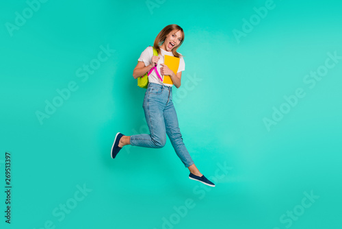 Full length side profile body size photo beautiful she her lady jump high arms hands hold back pack notebooks on way school friendly wear specs casual white t-shirt isolated teal green background