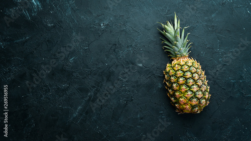 Pineapple on a black stone table. Tropical Fruits. Top view. Free space for your text.