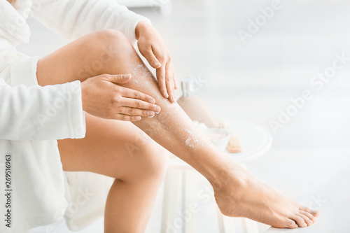 Beautiful young woman applying body scrub at home