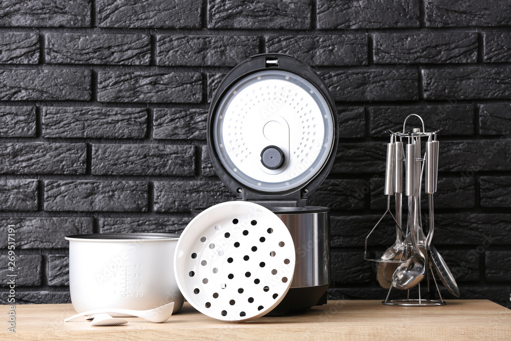 Modern multi cooker with accessories on table against dark background