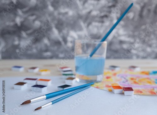 Watercolor paints and drawing supplies on a wooden table. 