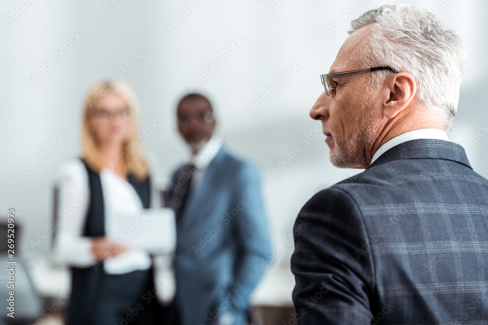 selective focus of man in glasses near multicultural colleagues selective focus of man in glasses near multicultural colleagues