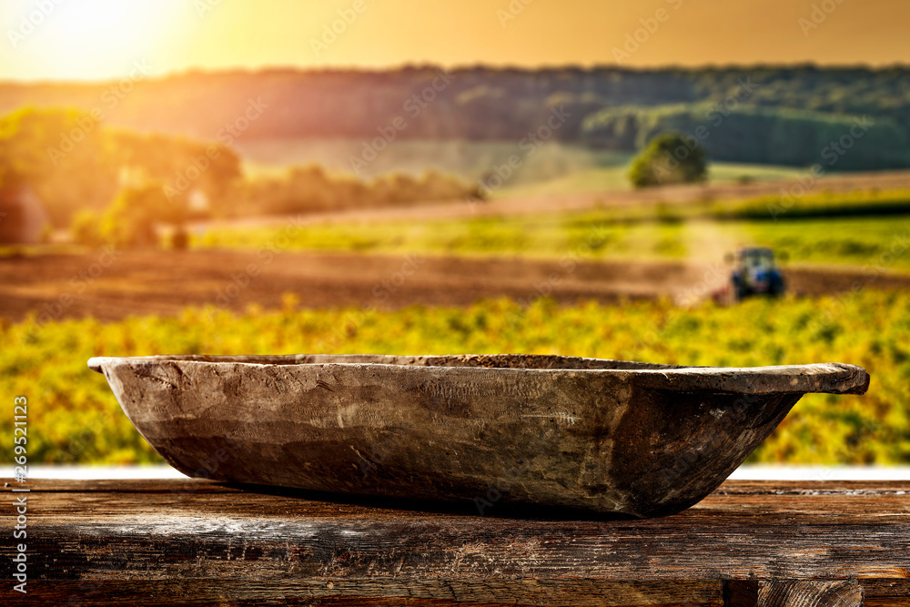 A wooden old destroyed bowl with space for your decoration. A large wooden table. Sunset in the countryside. Tractor cultivating the field. Summer time. A wooden old destroyed bowl with space for your decoration. A large wooden table. Sunset in the countryside. Tractor cultivating the field. Summer time.
