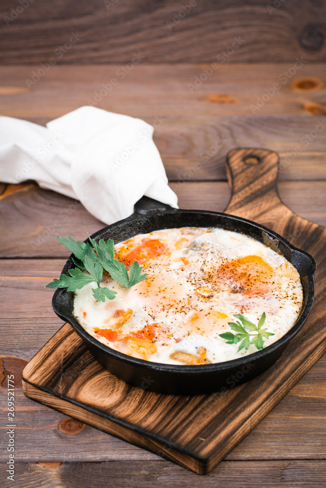 Homemade breakfast of shakshuka fried eggs with tomatoes and herbs in a pan on a wooden table Homemade breakfast of shakshuka fried eggs with tomatoes and herbs in a pan on a wooden table