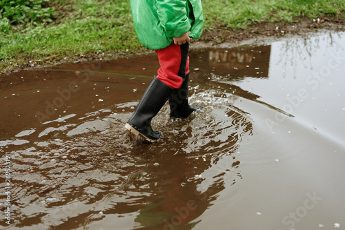  child walks after rain through the puddles in rubber boots