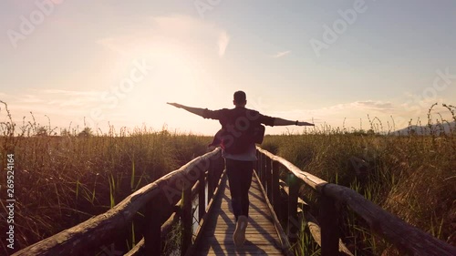 Ragazzo corre in libertà con le braccia aperte tipo aeroplano su un ponte di legno in mezzo alle piante. photo