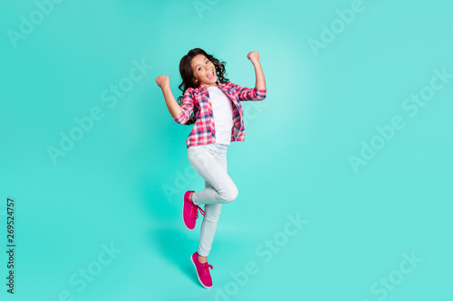 Full length body size view photo cute positive cheerful girl raise fist glad rejoice fortune summer holiday free time shout yeah energetic fan checked shirt sneakers trousers isolated green background