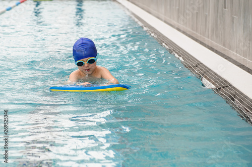 close up photo of 7-year boy swimming with a kickboad in the swiimming pool
