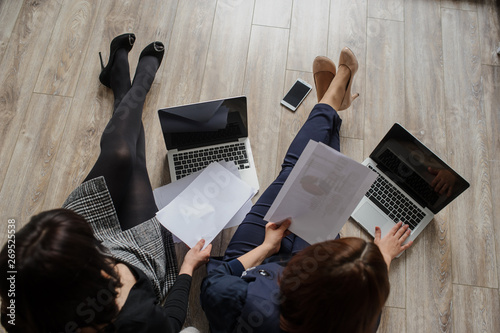 top view of two women in business outfit sitiing on the floor working on computers and discussing a report photo