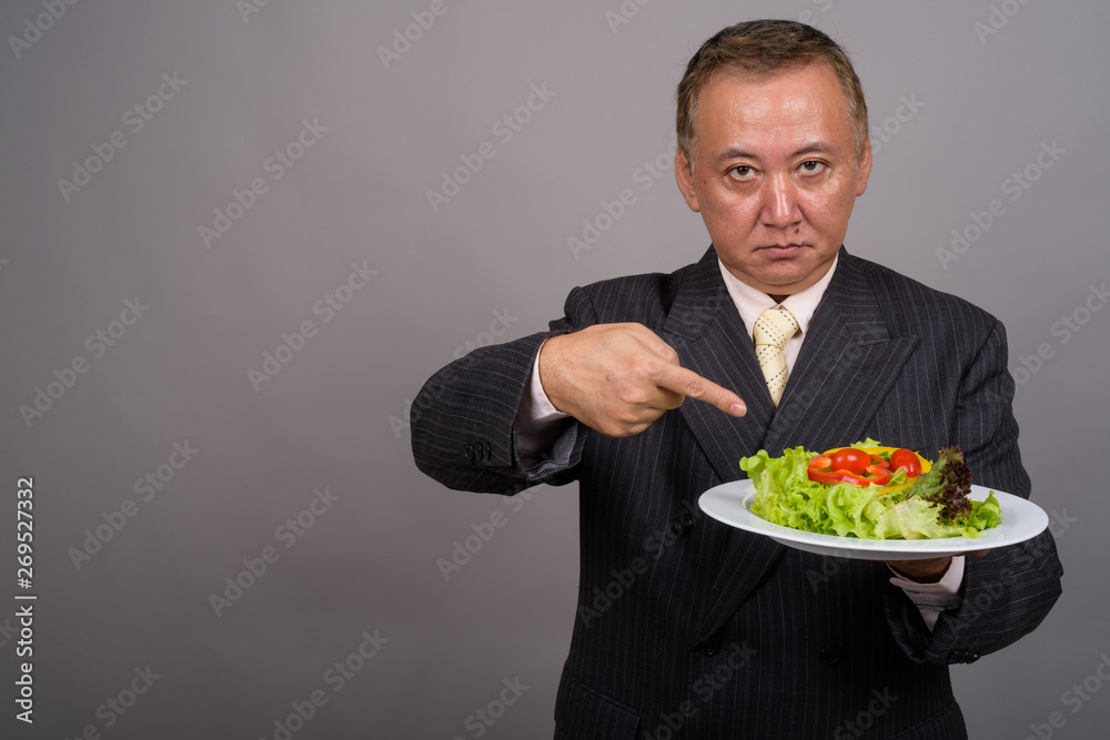 Portrait of mature Asian businessman against gray background Portrait of mature Asian businessman against gray background