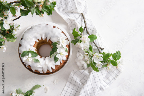 Homemade apple cake with cinnamon, white icing and flowering apple branches on white background. Pastry. Festive food. Spring mood. Top view, copy space