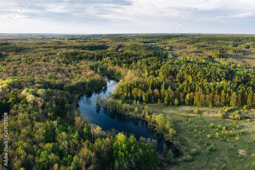 Aerial view of small blue lake among green forest trees on a calm sunny evening